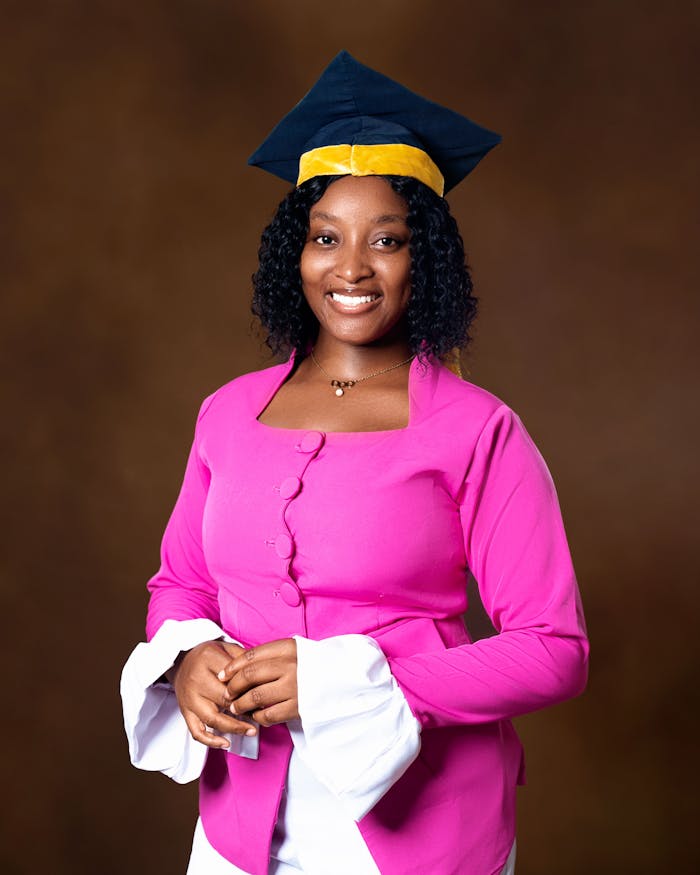 services-05 Portrait of a smiling graduate in a pink outfit and cap, celebrating achievement.