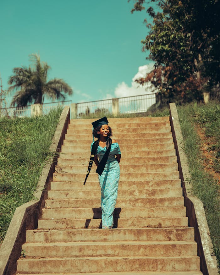 services-06 Young woman in graduation attire standing confidently outdoors on steps.