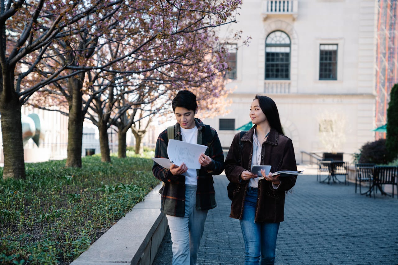 services-bg Two teenagers holding papers, walking through a campus courtyard during spring.