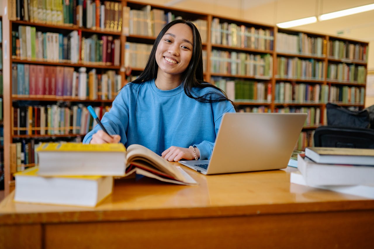 about-us Smiling student studying in a library with books and laptop, showcasing education and focus.